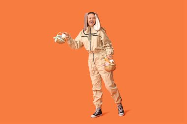 Turuncu arka planda Paskalya sepetleri olan tavşan kulaklı mutlu kadın arı yetiştiricisi.