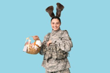 Mavi arka planda Paskalya sepeti olan tavşan kulaklı mutlu kadın asker.