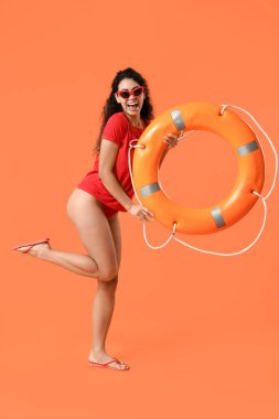 Turuncu arka planda halka şamandırası olan güzel, mutlu, Afro-Amerikan kadın cankurtaran.