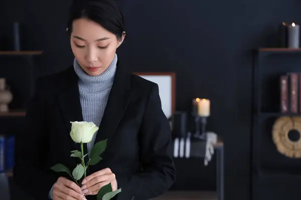 Mourning young Asian woman with white rose at funeral