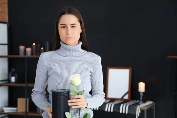 Mourning young woman with mortuary urn and rose at funeral