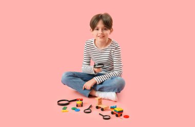 Little boy with magnifiers and toys on pink background clipart
