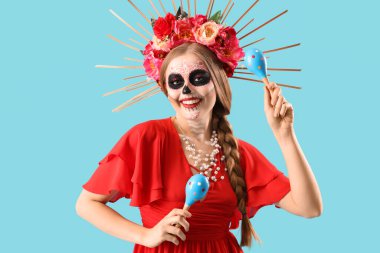 Yüzünde boyalı kafatası olan genç bir kadın mavi arka planda marakas tutuyor. Meksika Ölüler Günü 'nün Kutlaması (El Dia de Muertos)