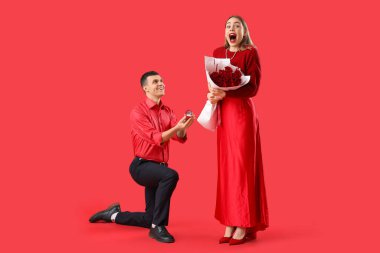Yüzüklü genç adam kırmızı arka planda sevgilisine evlenme teklif ediyor. Sevgililer Günü kutlaması