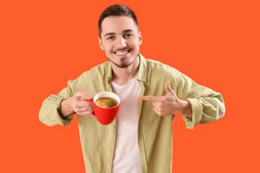 Genç adam turuncu arka plandaki bir bardak limon çayını işaret ediyor.