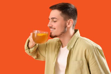 Turuncu arka planda bir bardak limon çayı olan genç adam.