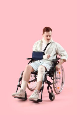 Pembe arka planda tekerlekli sandalyede kaza sonucu yaralanan genç adam.