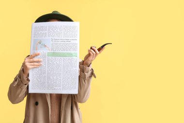 Pelerinli kadın, sarı arka planda sigara piposu içiyor.