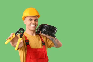 Young male electrician with wire crimper and flexible conduit tube on green background clipart