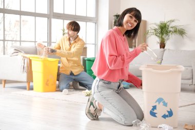 Oturma odasındaki çöpleri düzenleyen çöp konteynırları olan genç çift. Geri dönüşüm kavramı