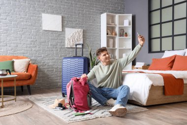 Sırt çantalı erkek turist otel odasında selfie çekiyor.