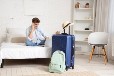 Otel odasında cep telefonuyla konuşan dizüstü bilgisayarlı bir erkek turist.