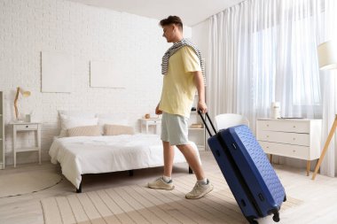 Bavullu bir erkek turist otel odasında yürüyor.