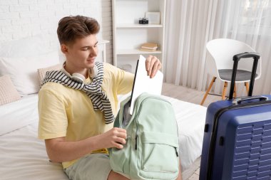 Erkek turist otel odasında sırt çantasından laptop alıyor.