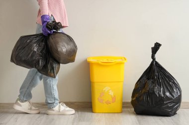 Beyaz duvarın yanında çöp torbası ve çöp kutusu olan bir kadın.