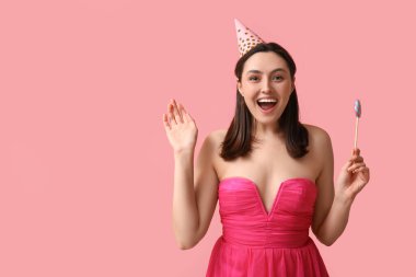 Pembe arka planda tatlı lolipopu olan parti şapkalı mutlu genç kadın.