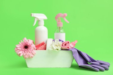Yeşil zemin üzerinde temizlik malzemeleri, aletler ve bahar çiçekleri olan sepet.