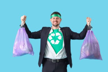 Mavi arka planda çöp torbaları olan bir süper kahraman gibi giyinmiş genç adam. Ekoloji kavramı