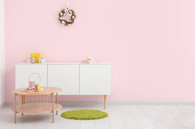Güzel Paskalya çelengi oda çekmecesinin yanındaki pembe duvarda yumurtalarla süslenmiş.