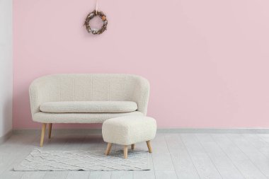 Yeşil duvarda güzel Paskalya çelengi ve şık oturma odasında rahat bir kanepe.