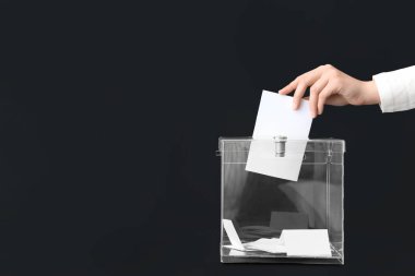Siyah arka planda oy sandığının yanında oy veren kadın