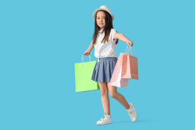 Mavi arka planda alışveriş torbaları olan şık küçük bir kızın portresi