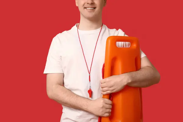 Male lifeguard with rescue tube buoy and whistle on red background