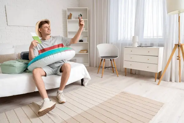 Male tourist with passport and swim ring taking selfie in hotel room