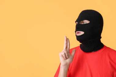 Kar maskeli yakışıklı genç adam sarı arka planda silah işareti gösteriyor.