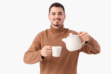 Genç adam beyaz arka planda fincana çay dolduruyor.