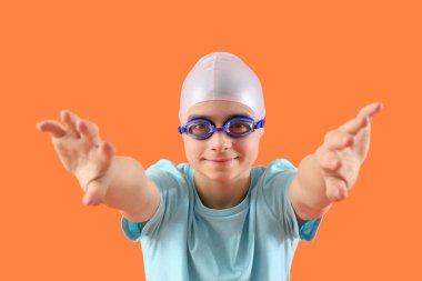 Yüzme şapkası ve turuncu arka planda gözlüğü olan şirin, mutlu bir çocuk.