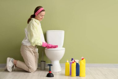 Yeşil duvarın yanındaki klozeti temizleyen genç kadın.