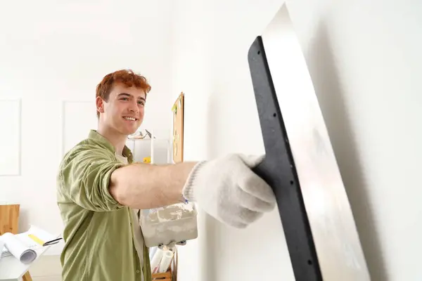 Young man with putty knife working at home