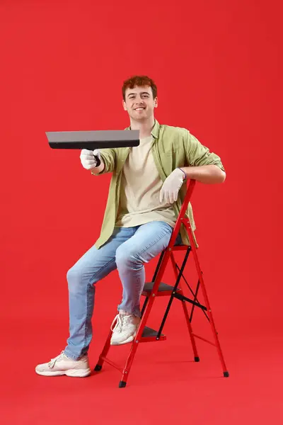 Young man with putty knife on red background
