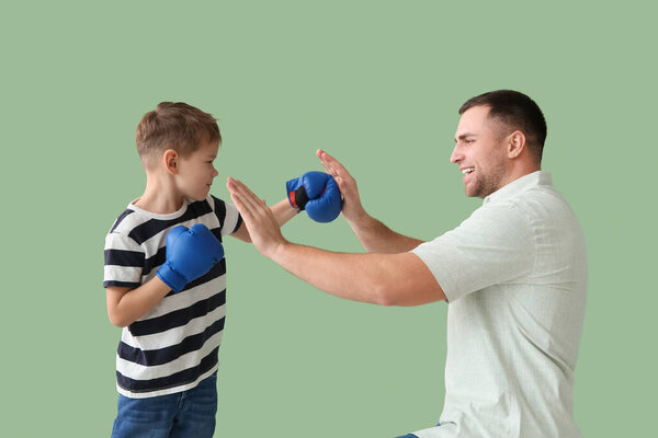 Happy father and his little son during boxing training on green background