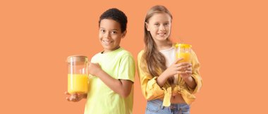 Turuncu arka planda bir sürahi taze narenciye suyu ve fincanlı küçük çocuklar.