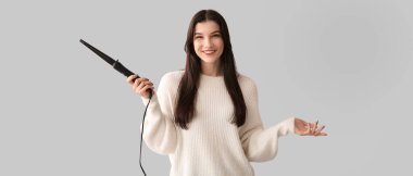 Gri arka planda saç maşası olan güzel mutlu kadın.