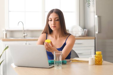 Mutfaktaki masada vitamin takviyesi ve dizüstü bilgisayarı olan güzel bir kadın.