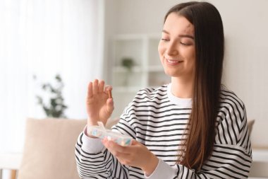Young woman holding container with vitamin supplements at home