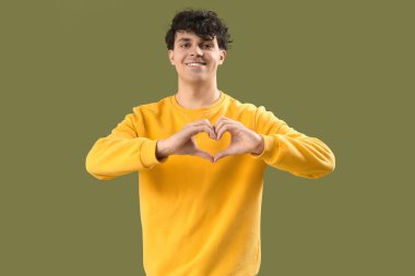 Yakışıklı genç adam, elleri yeşil arka planda kalp yapıyor.