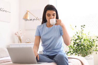 Dizüstü bilgisayarı olan, yatak odasında kahve içen serbest bir kadın.