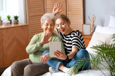 Büyükannesiyle birlikte yatak odasında tablet bilgisayar kullanan genç bir kadın.