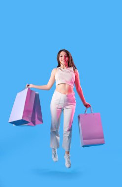 Alışveriş çantalı genç bir kadın mavi arka planda zıplıyor