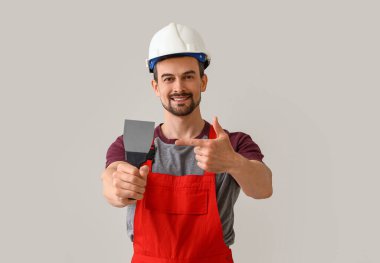 Erkek dekoratör arka plandaki macun bıçağını işaret ediyor.