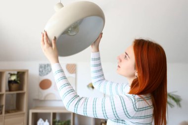 Güzel genç bir kadın evinde ampulü değiştiriyor.