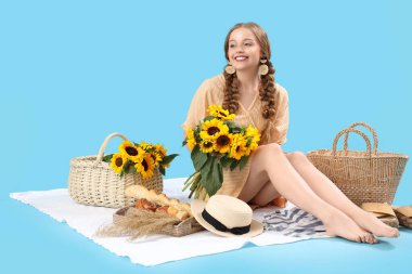 Güzel ayçiçekleri olan genç bir kadın mavi arka planda piknik yapıyor.
