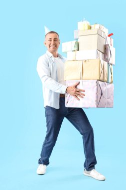 Mavi arka planda doğum günü hediyesi olan parti şapkalı olgun bir adam.