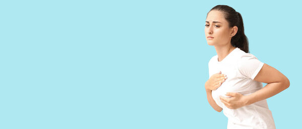 Young woman suffering from breast pain on light blue background with space for text. Cancer awareness concept