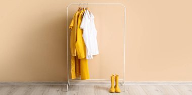 Şık kıyafetler ve bej duvarın yanında lastik çizmelerle dizilin.