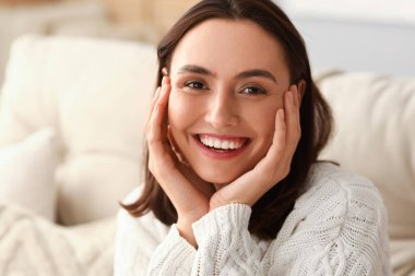 Evde kalın kazaklı genç bir kadın, yakın plan.